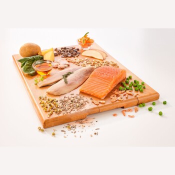 Ein Holzschneidebrett zeigt frischen Lachs und weiße Fischfilets, umgeben von Gemüse wie Kartoffeln und Salat, Nüssen, Samen und Kräutern.