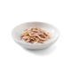Eine weiße Schüssel gefüllt mit zerriebenem, feuchtem Katzenfutter, mit hellrosa und beigen Fleischstücken in einer cremigen Sauce.
