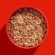 Eine rote Schüssel, gefüllt mit Haustierfutter, das eine Mischung aus Hackfleisch, kleinen Gemüsestücken und gebogenen Pastaformen enthält.