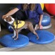 Ein brauner und weißer Hund steht auf zwei blauen Balance-Discs und trägt ein gelbes Geschirr. Eine Frau interagiert sanft mit dem Hund.