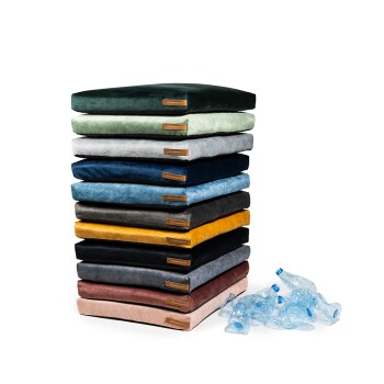 Ein Stapel bunter Haustierkissen in verschiedenen Farbtönen, darunter Grün, Grau, Blau und Gelb, mit einigen blauen Plastikflaschen daneben.