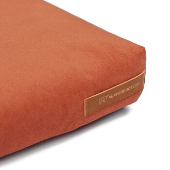 Eine Nahaufnahme eines rostfarbenen Haustierbettes mit weicher Textur, das ein Etikett mit der Aufschrift "RexProduct.com" trägt.