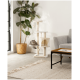 Ein gemütliches Wohnzimmer mit einem beigen Kratzbaum für Katzen, auf dem eine getigerte Katze auf einer Plattform liegt, einer Topfpflanze und einem grauen Sofa.