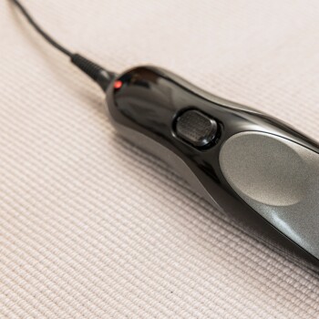 Zwart-grijze elektrische huisdierverzorgingsclipper met stroomkabel op een gestructureerd beige oppervlak.