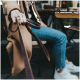 Eine Person hält eine braune Lederhundeleine, trägt einen Ring, sitzt in einem Café mit einem lässigen Outfit aus einem beigen Mantel und blauen Jeans.