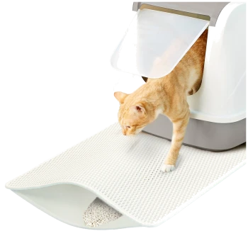 Eine hellorangefarbene getigerte Katze kommt aus einer modernen Katzentoilette auf eine strukturierte weiße Matte, die Streu auffängt.