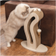 Un chat crémeux et duveteux gratte un grattoir moderne en bois avec un design incurvé, comportant un jouet suspendu, à côté d'un canapé marron.