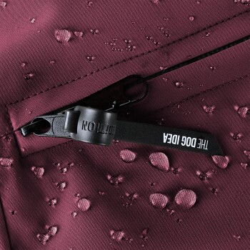 Nahaufnahme eines kastanienbraunen wasserdichten Stoffes mit Wassertropfen, mit einem Reißverschluss und einem Etikett, das "THE DOG IDEA" liest.