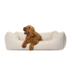 Ein plüschiges, beiges Hundebett mit geripptem Stoff und erhöhten Rändern, entworfen für Komfort und Unterstützung.