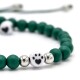 Grünes, perlenbesetztes Haustierarmband mit einer weißen Perle mit einem schwarzen Pfotenabdruck und Herzdesign, vor einem verschwommenen Hintergrund.