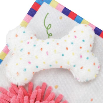 Un jouet en peluche doux et blanc en forme d'os, décoré de pois colorés, placé sur un fond à motifs vibrants.