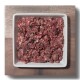 Ein quadratisches weißes Geschirr, gefüllt mit rohem, fein gehacktem rotem Fleisch, auf einer Holzoberfläche platziert.