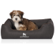 Ein kleiner, flauschiger Hund sitzt bequem in einem dunkelbraunen Haustierbett, auf dem das Logo "KNUFFELWUFF" deutlich auf der Vorderseite angezeigt wird.