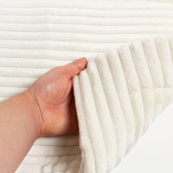 Eine Hand hält eine weiche, weiße Haustierdecke mit gerippter Textur, die ihren plüschigen Stoff und ihr gemütliches Aussehen zeigt.