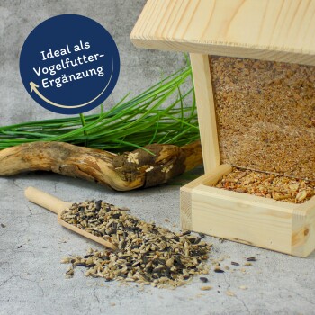 Futterstation aus Holz und Schaufel mit gemischtem Vogelfutter auf Beton; blaues Siegel mit der Aufschrift „Ideal als Vogelfutter-Ergänzung“
