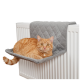 Eine orange getigerte Katze, die auf einem grauen, gesteppten Heizkörperbett liegt, das auf einem weißen Heizkörper positioniert ist.