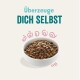Bol de nourriture pour animaux de compagnie rempli de croquettes brunes, avec le texte "Überzeuge DICH SELBST" au-dessus en turquoise et rose gras.