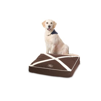 Ein Golden Retriever sitzt neben einem plüschigen, braunen Hundebett mit einem weißen Kreuzdesign.