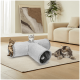 Zwei verspielte Katzen, eine getigerte und eine graue, erkunden einen weichen grauen Tunnel in einem gemütlichen Wohnzimmer mit einem beigen Sofa und einer Pflanze.