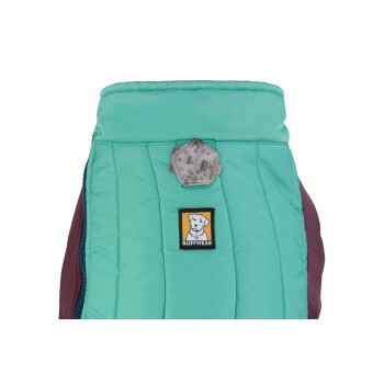 Eine Nahaufnahme einer türkisfarbenen und kastanienbraunen Hundejacke mit einem Ruffwear-Logo-Patch und einem reflektierenden Lichtanhänger am Kragen.