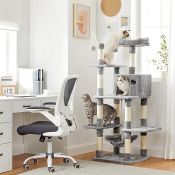 Ein modernes Homeoffice mit einem weißen Schreibtisch und einem ergonomischen Stuhl, mit einem hohen grauen Kratzbaum, auf dem drei Katzen spielen und sich entspannen.