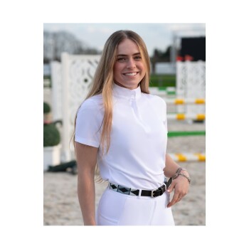 Eine junge Frau in einem weißen Reitshirt und eng anliegenden weißen Hosen steht selbstbewusst da, trägt einen schwarzen Gürtel mit einem dekorativen Muster.