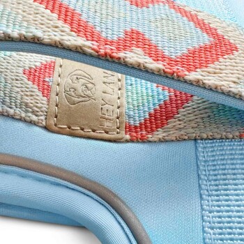 Nahaufnahme eines blauen Haustiergeschirrs mit einem bunten gewebten Riemen mit roten und hellblauen Mustern, beschriftet mit "HEY LA."