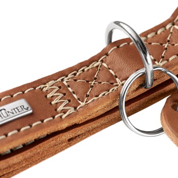 Nahaufnahme eines braunen Lederhalsbands mit cremefarbener Naht, Metall-D-Ringen und Metallanhänger mit der Aufschrift „HUNTER“