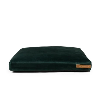 Ein plüschiges, dunkelgrünes Hundebett mit einer glatten Oberfläche und einem kleinen braunen Etikett mit der Aufschrift 'rexproduct.com' an der Seite.