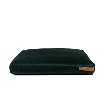 Ein plüschiges, dunkelgrünes Hundebett mit einer glatten Oberfläche und einem kleinen braunen Etikett mit der Aufschrift 'rexproduct.com' an der Seite.