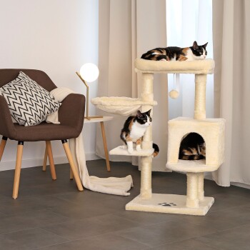 Gemütliches Wohnzimmer mit einem beigen Katzenbaum, zwei schildpattfarbenen Katzen, einem stilvollen Stuhl und einer Lampe. Eine Katze entspannt oben, eine andere auf einer mittleren Plattform.