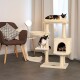 Gemütliches Wohnzimmer mit einem beigen Katzenbaum, zwei schildpattfarbenen Katzen, einem stilvollen Stuhl und einer Lampe. Eine Katze entspannt oben, eine andere auf einer mittleren Plattform.