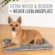 Ein brauner Hund ruht auf einem weichen, grauen Haustierbett. Der Text darüber lautet 'EXTRA WEICH & BEQUEM = NEUER LIEBLINGSPLATZ.'