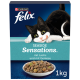 Un chat noir et blanc allongé à côté d'une boîte de nourriture pour chat Purina Felix Seaside Sensations, contenant des croquettes avec du poisson et des légumes, 1 kg.