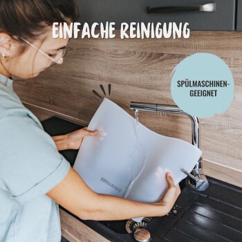 Eine Person wäscht eine durchsichtige Futtermatte für Haustiere unter einem Wasserhahn, mit den Etiketten "EINFACHE REINIGUNG" und "SPÜLMASCHINEN-GEEIGNET."