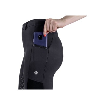 Eine Nahaufnahme einer Hand einer Frau, die ein Smartphone in die Gesäßtasche von schwarzen Reithosen steckt, die ein Logo an der Seite haben.