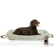 Ein brauner Labrador Retriever liegt bequem auf einem gemütlichen, gewebten Haustierbett mit einem cremefarbenen Kissen, neben einem beigen Haustierzubehör.