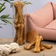 Ein Glasbehälter, gefüllt mit großen, kaubaren Hundeknochen, steht neben einem rosa Haustiersofa, mit zwei weißen Seilspielzeugen und einer Holzscheibe auf einem Holztisch.