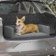 Ein glücklicher Corgi liegt auf einem grauen Haustiersitz im Rücksitz eines Autos, mit einem strukturierten schwarzen Hintergrund und sichtbarem Grünzeug draußen.