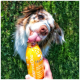 Ein schwarzer Hund trinkt aus einer blauen Flasche mit dem Etikett "Trinkpause" und dem Text "Erfrischt jeden Hund" an einem sandigen Strand.