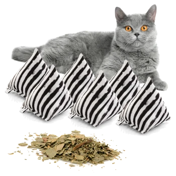Eine graue Katze mit leuchtend orangefarbenen Augen liegt neben fünf gestreiften Katzenminzkissen und einem Haufen getrockneter Katzenminzblätter.