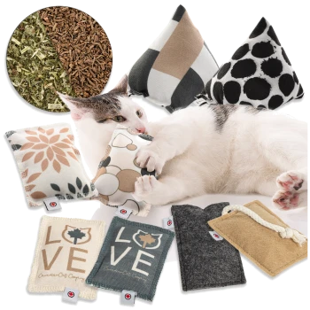 Eine verspielte Katze kuschelt mit verschiedenen bunten Katzenminze-Spielzeugen, mit floralen und geometrischen Mustern, vor einem Hintergrund aus getrockneten Kräutern.