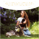 Eine Frau mit einer schwarzen Katze sitzt neben einem wolfähnlichen Hund in einem Garten mit lila Blumen. Text oben bewirbt Wolfsbacher Naturprodukte.