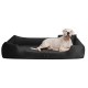 Ein weißer Hund, der auf einem plüschigen schwarzen Hundebett mit erhöhten Rändern liegt, mit einem kleinen Logosticker auf der Vorderseite.
