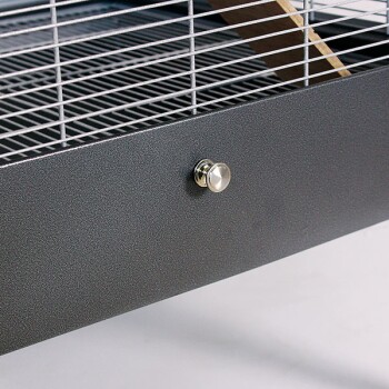 Nahaufnahme eines Haustierkäfigs mit einem Metallgitteroberteil und einem eleganten dunkelgrauen Boden mit einem glänzenden runden Knopf für den Zugang.