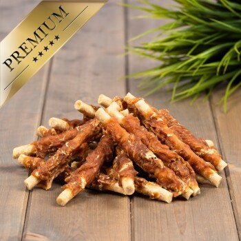 Ein Haufen hochwertiger Hundeleckereien aus gedrehtem Fleisch, das um Rohhautstangen gewickelt ist, auf einer Holzoberfläche mit grünem Gras im Hintergrund.