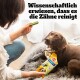 Eine Person hält einen grünen Hundezahnpflege-Kauknochen neben einer Pedigree Dentastix-Packung mit einem Hund und Text über die Zahnreinigung.