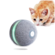 Eine neugierige orangefarbene Tabby-Katze schnüffelt an einem grauen, flauschigen interaktiven Spielzeugball mit einem grünen Licht und einem Knopf, der mit "Cheerble" beschriftet ist.