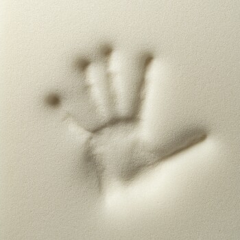 Ein Handabdruck, der in feinen, hellen Sand gedrückt wurde, der die Details der Finger und der Handfläche vor einem glatten Hintergrund zeigt.