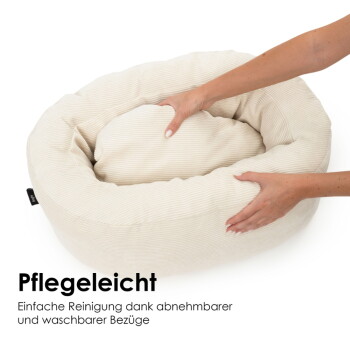 Cremefarbenes, rundes Cord-Haustierbett mit herausnehmbarem Innenkissen, Hände richten es; sichtbarer Text „Pflegeleicht“ und ein deutscher Reinigungshinweis.